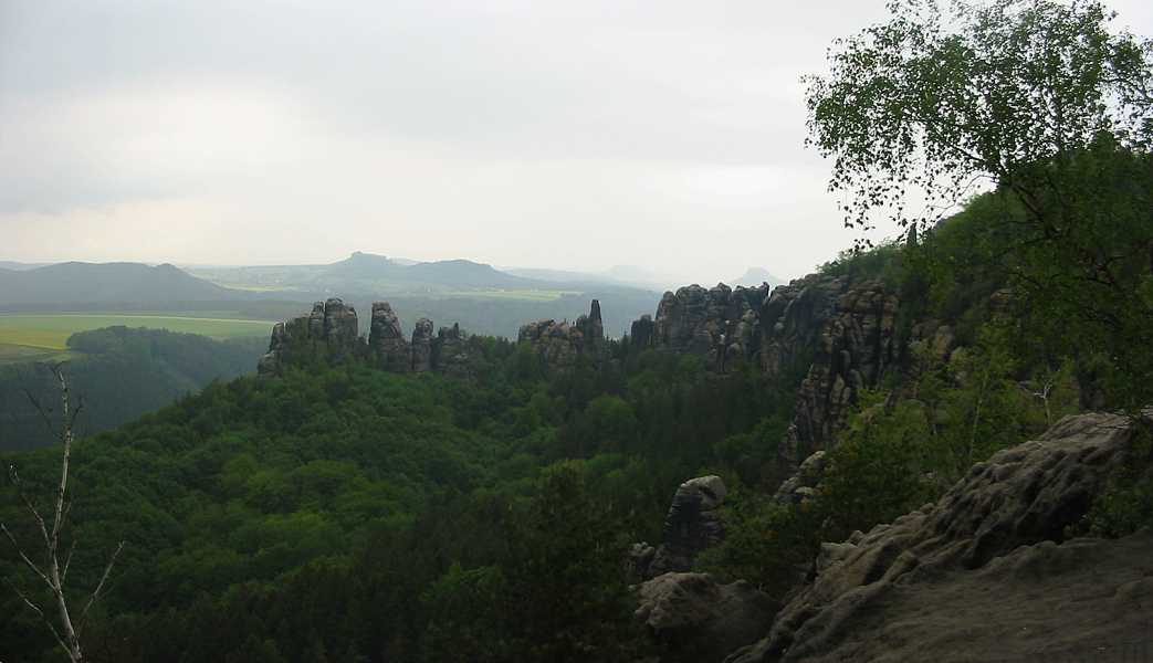 Die Aussicht vom Gratweg aus in Richtung Nord-West mit dem Schrammsteinmassiv, dabei das Große Schrammtor. In der Ferne sind die Festung Königstein und der Lilienstein zu erkennen.