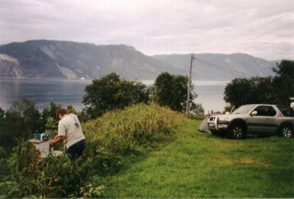 Hinter dem Waschbecken geht es f&uuml;nf Meter steil hinunter zum rauschenden Wildwasserflu&szlig;, in der Ferne auf dem Fjord f&auml;hrt ein Schiff.