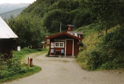Vor uns liegt die Rezeption. Dahinter geht es zu den H&uuml;tten, die Zeltplatzwiese liegt hinter uns. Um das linke Geb&auml;ude herum kommt man zum Sanit&auml;rgeb&auml;ude. Links vor dem Geb&auml;ude f&uuml;hrt der Weg zum Fjord hinunter.