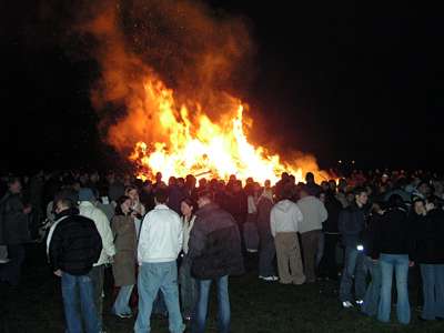 Ins Feuer schauen, sich treffen und unterhalten - eine Menge Menschen stehen rings um das Feuer. Es herrscht eine fr&ouml;hliche Stimmung.